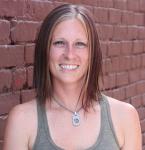 a woman, smiling at the camera in front of red brick wall