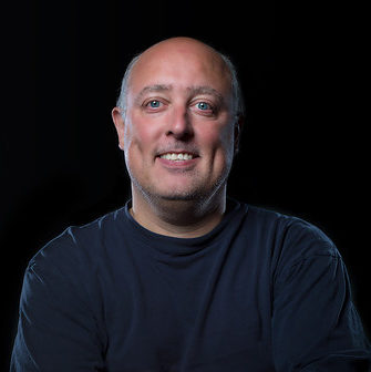 headshot photo of a man smiling in a black background