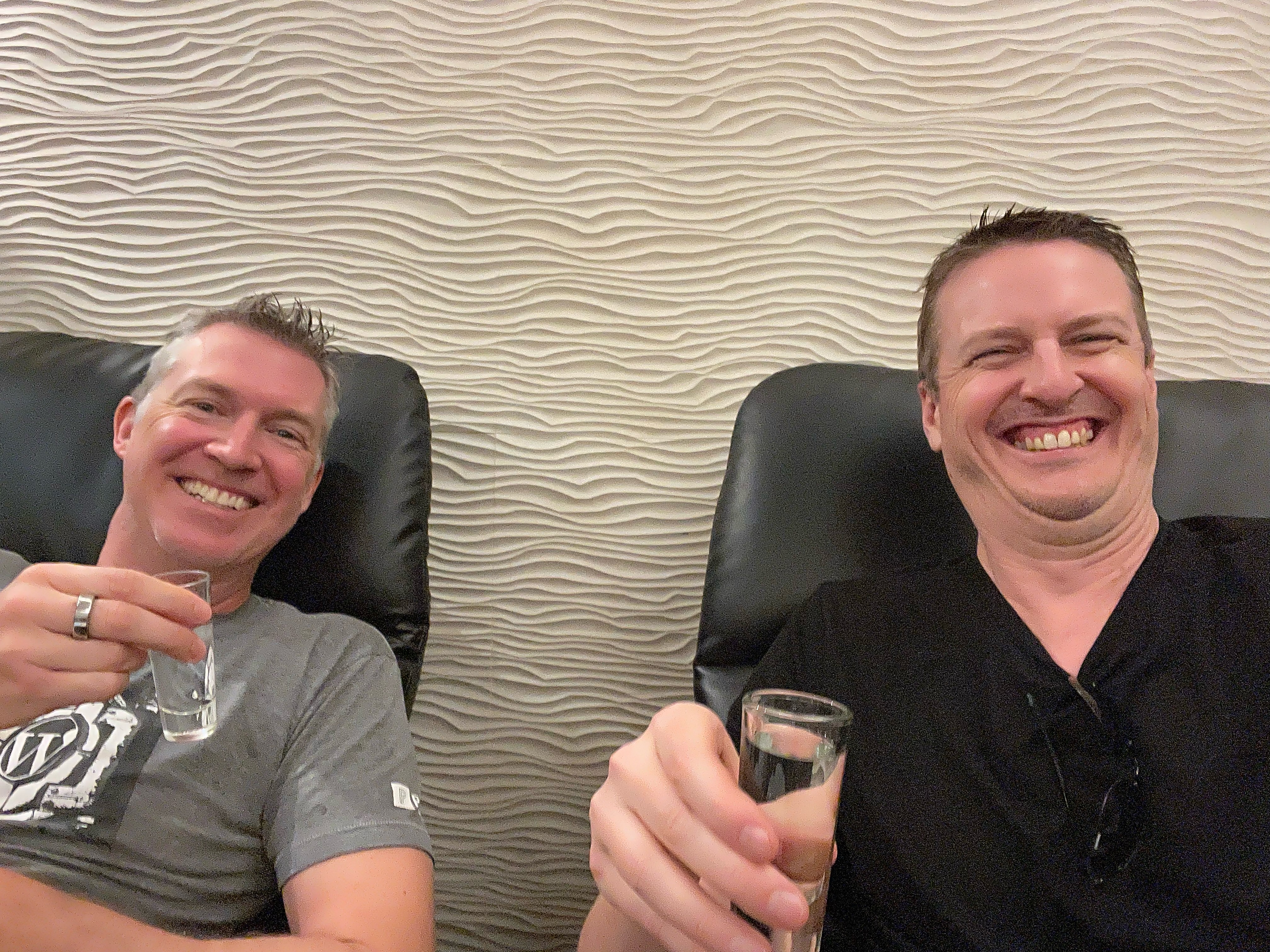 two men sitting on a chair holding a glass of vodka having a relaxing moment